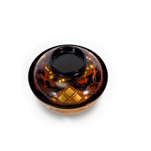 The lidded bowl from a high angle, the black knob at the lid's centre, red pine lines and gold lattice on the near side.
