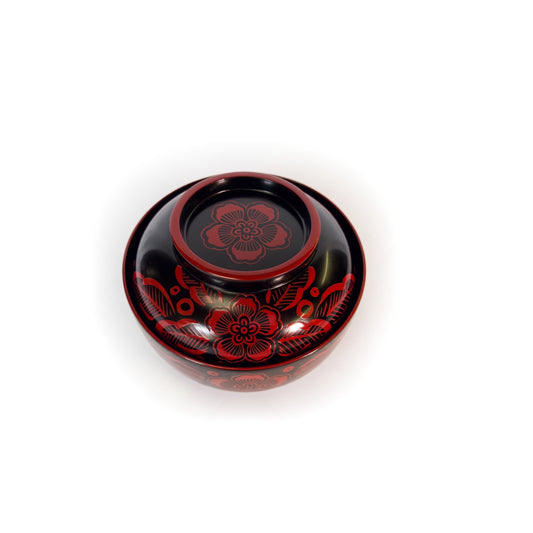 The lidded bowl from a high angle, the raised red-rimmed disc on top of the lid with a single red blossom painted on it.