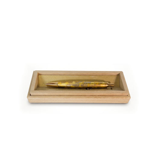The pen lying flat in the open wooden box, gold-toned lining beneath it and the tapered tip pointing left.