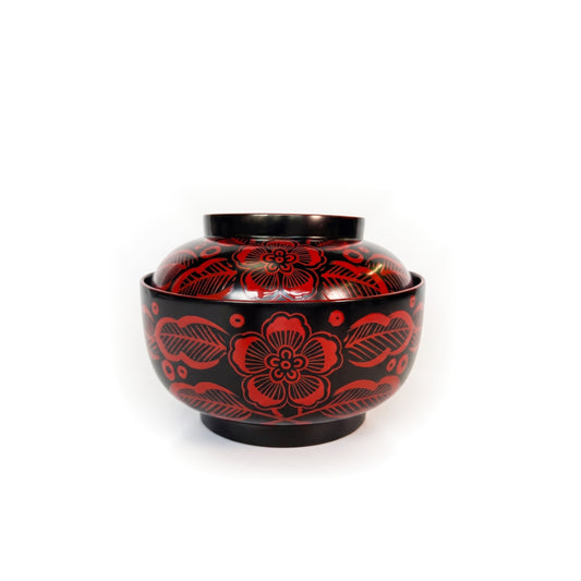 A black lacquer lidded bowl from the front, five-petalled blossoms and hatched leaves painted in red across the lid and body.