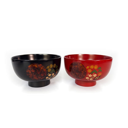 A black soup bowl and a red soup bowl side by side on raised feet, each with a mottled copper circle and painted flowers.