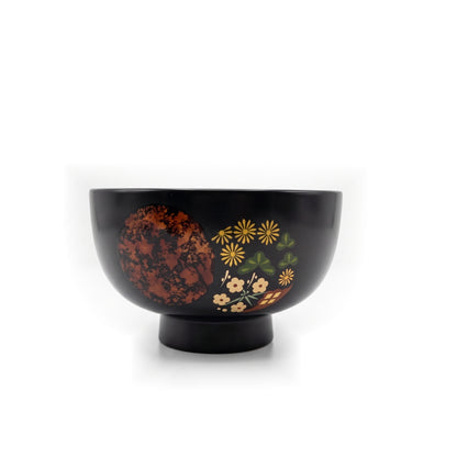 A single black soup bowl on a raised foot, its mottled copper circle beside yellow chrysanthemums, pine, and plum blossoms.