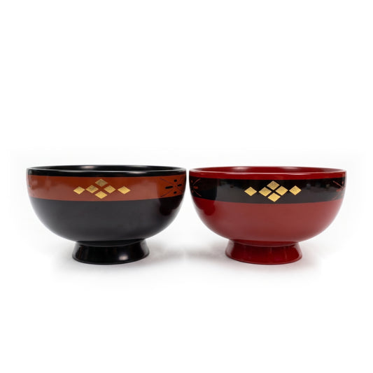 A black lacquer bowl and a red lacquer bowl side by side, each on a high foot, with a gold-diamond band near the rim.