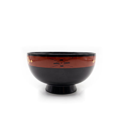 A black lacquer bowl on a high foot, with a dark cross-and-dot motif on its rust-toned band and gold diamonds at the edges.