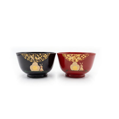 A pair of child-sized lacquer soup bowls, one black and one red, each with a rabbit and blossom under scattered gold leaf.