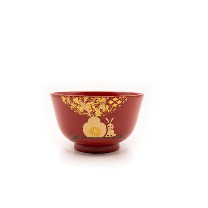 The red bowl seen from the front, the rabbit and blossom with green grass at their feet, under scattered gold leaf.
