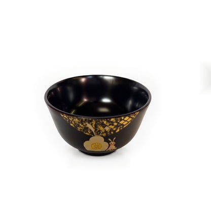 The black bowl from a higher angle, its glossy dark interior in view, scattered gold leaf near the rim.