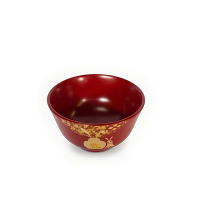 The red bowl from a higher angle, its red interior in view, the blossom and rabbit's ears at the lower edge.