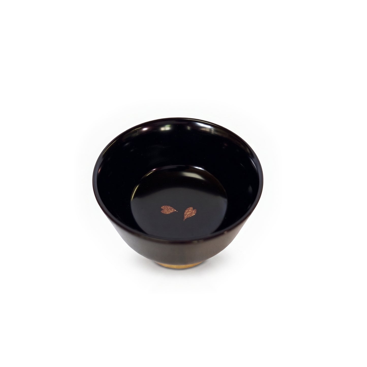 A single black lacquer cup from above, its glossy black interior holding two bronze cherry blossom petals left of centre.