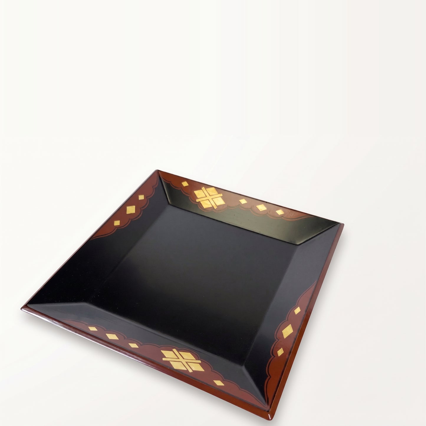 Tray viewed at a steep angle, one corner toward the camera, black surface receding, gold-diamond border on all sides.