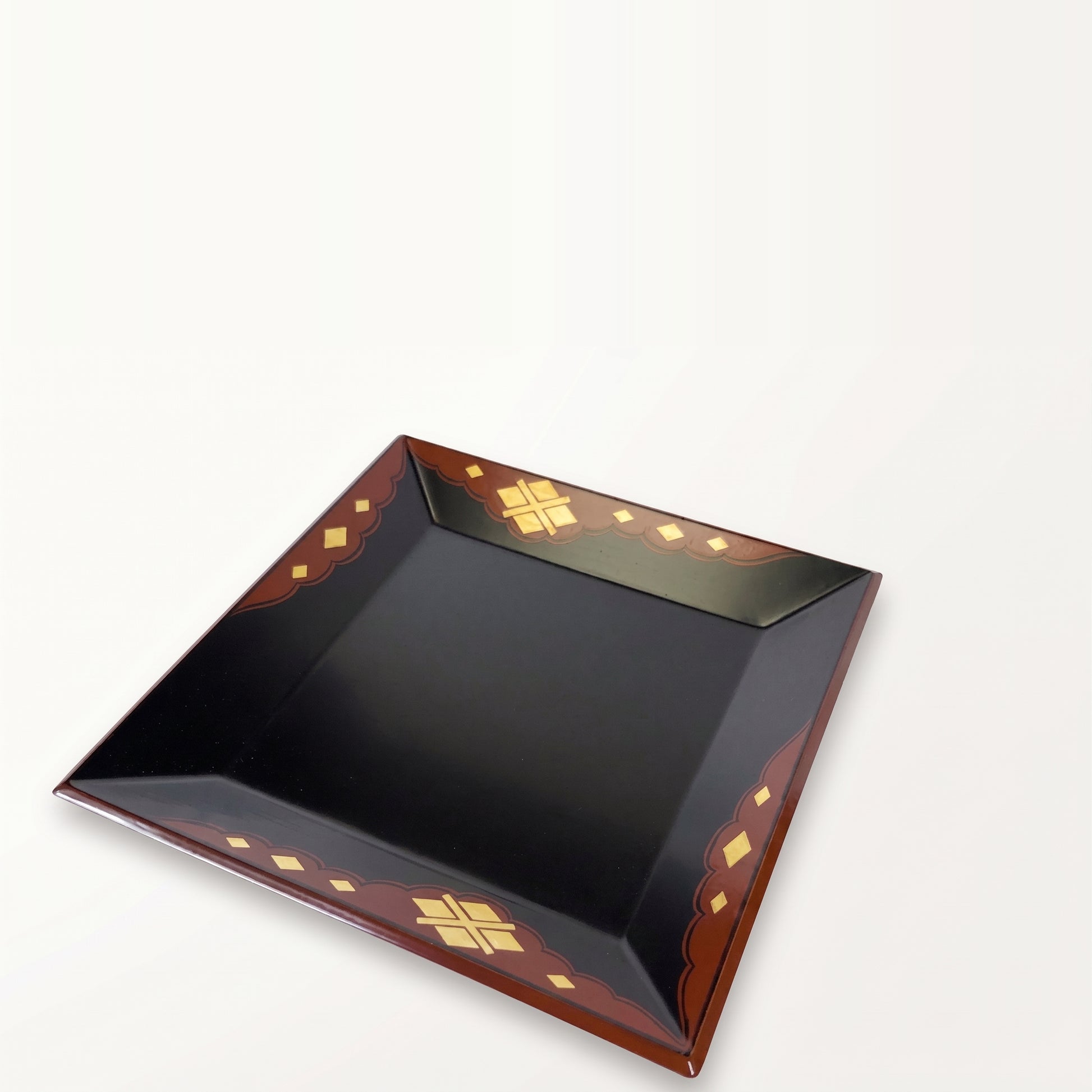 Tray viewed at a steep angle, one corner toward the camera, black surface receding, gold-diamond border on all sides.
