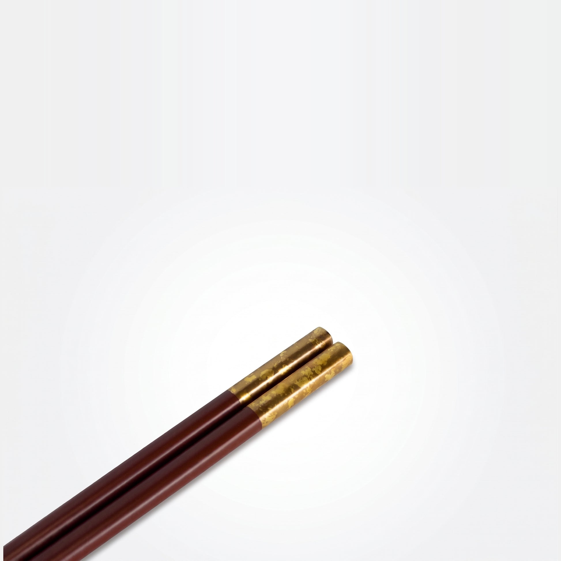 Close-up of the deep red pair's gold-leaf grip ends, showing the uneven, cloud-like texture of the applied leaf.