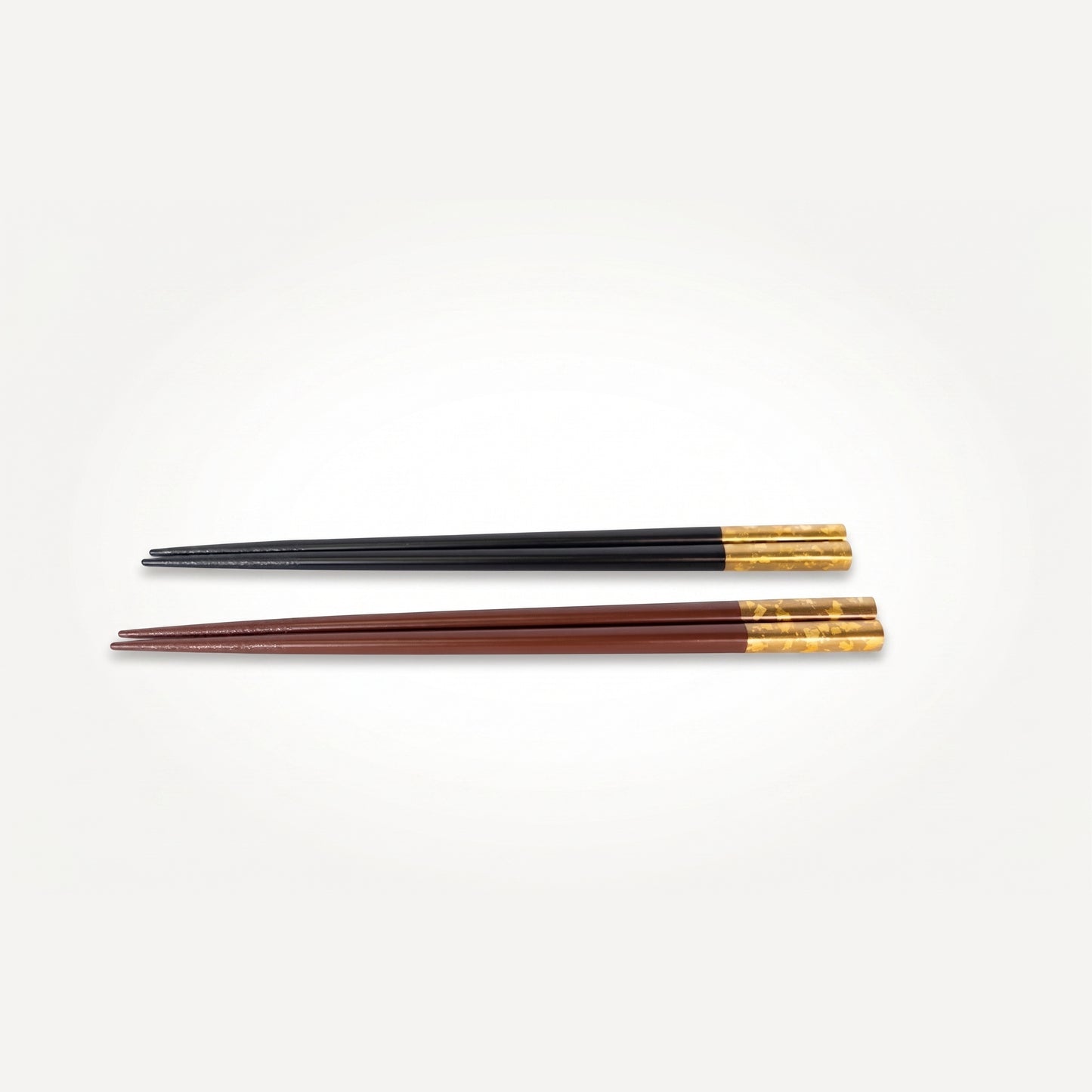 Two Hidehira-nuri chopstick pairs, one black and one deep red, lying side by side with gold leaf near the grip end.