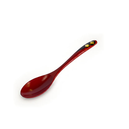 The red spoon alone on the same diagonal, its two gold diamonds resting on a black cloud shape that tapers down the handle.